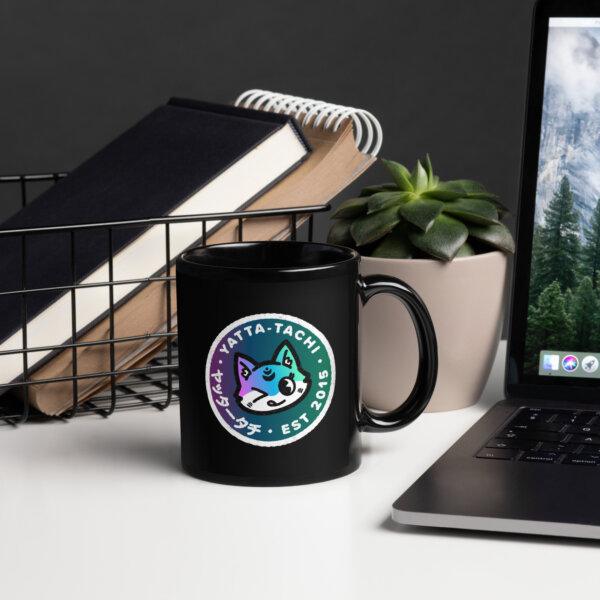 A black mug with the Hachi emblem sitting on the desk next to a computer and other decor.